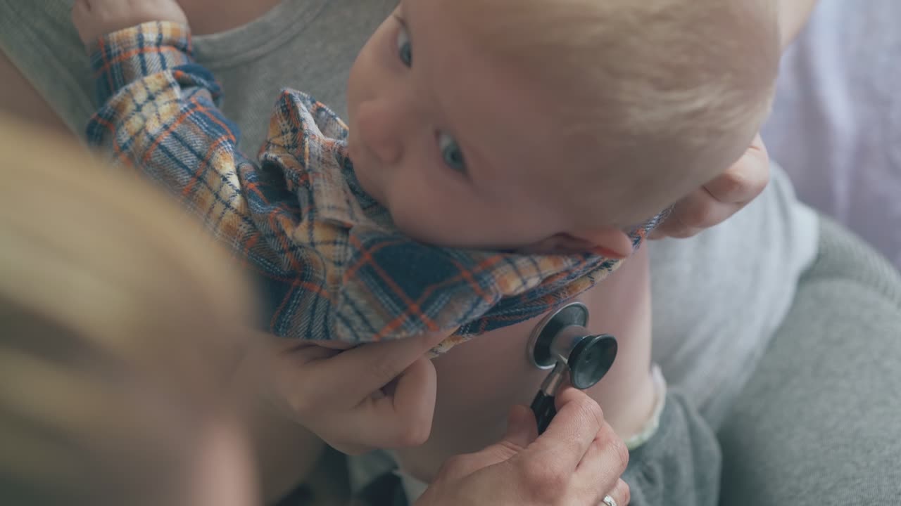 소아과 의사는 침대에 있는 엄마의 도구로 아기의 폐를 듣습니다.