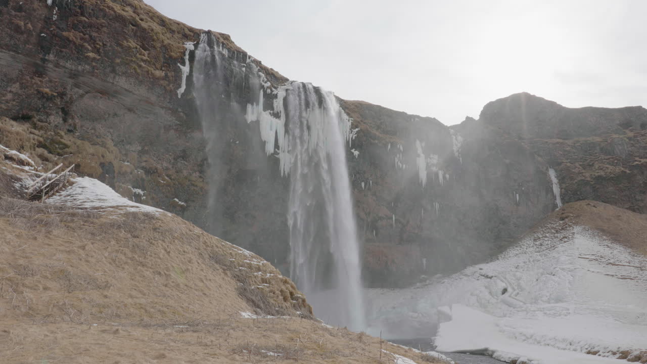 cascada de seljalandsfoss, islandia, hito natural en la temporada de primavera, agua glacial y hielo bajo un acantilado.