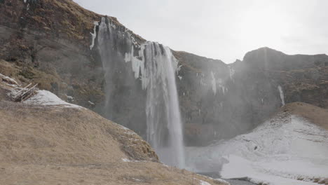 Seljalandsfoss-Waterfall,-Iceland,-Natural-Landmark-in-Spring-Season,-Glacial-Water-and-Ice-Under-Cliff
