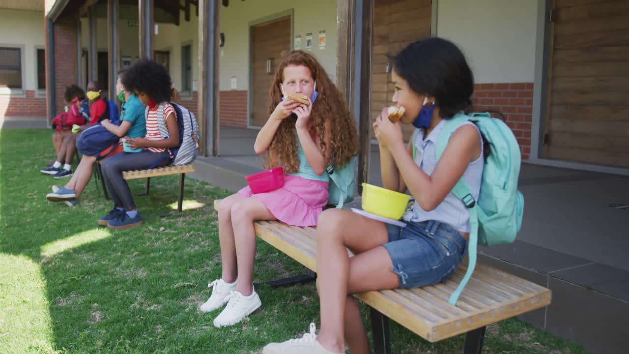 dos niñas comiendo el almuerzo de la caja de tiffin mientras están sentadas en un banco en el parque en la escuela
