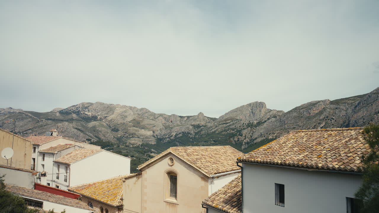 Vista sui tetti tradizionali in tegole in un villaggio mediterraneo con una catena montuosa imponente sullo sfondo. Combinazione scenografica di architettura e natura