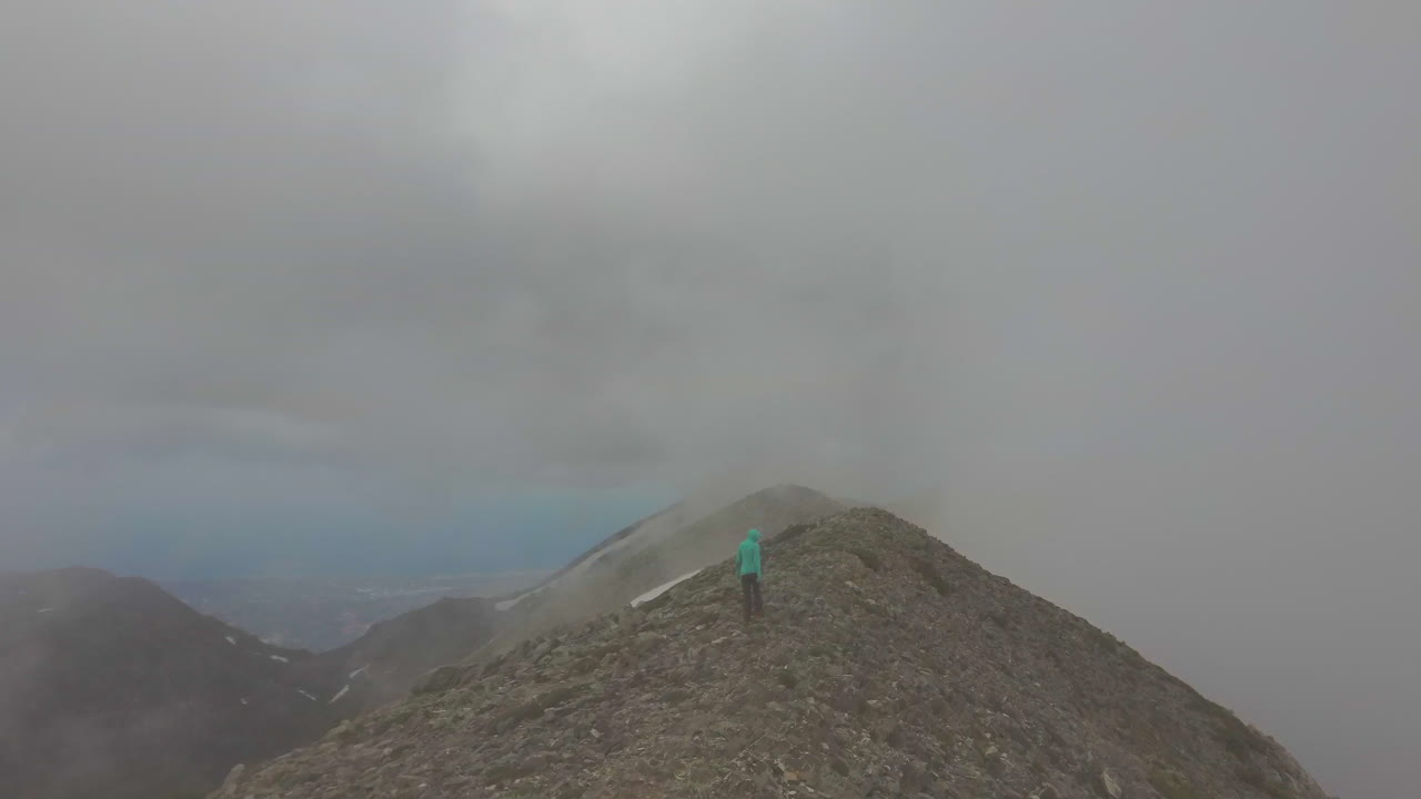Aerial view of a hike girl that walks on a mountain peak during a foggy day. Hiker on the top of mountain and drone reveals the landscape. Travel and freedom concept in 4k
