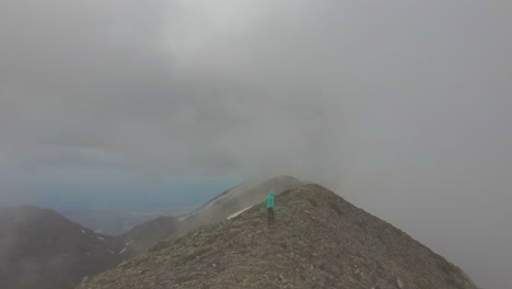 aerial view of a hike girl that walks on a mountain peak during a foggy day. hiker on the top of mountain and drone reveals the landscape. travel and freedom concept in 4k