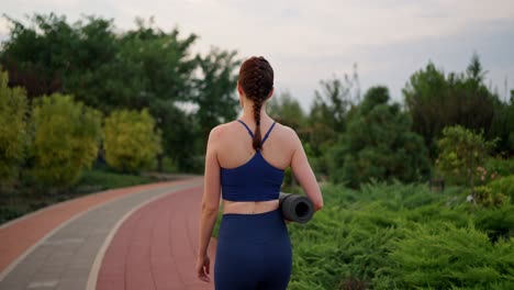 woman walking in park with yoga mat