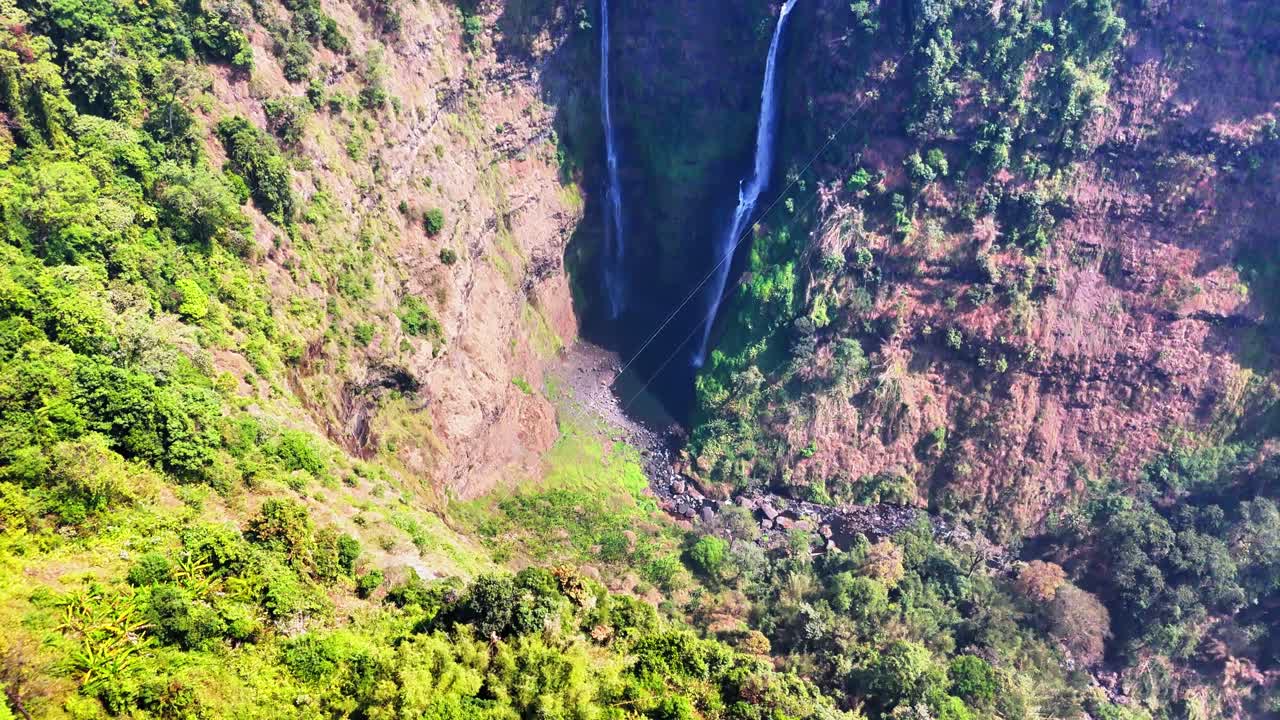 Steep drone reveal unveils the majestic twin streams of Tad Fane Waterfall plunging into a deep gorge amid lush rainforest on the Bolaven Plateau in Champasak Province, southern Laos