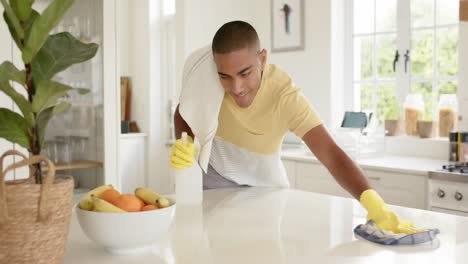 Happy-biracial-man-cleaning-countertop-in-bright-kitchen,-slow-motion