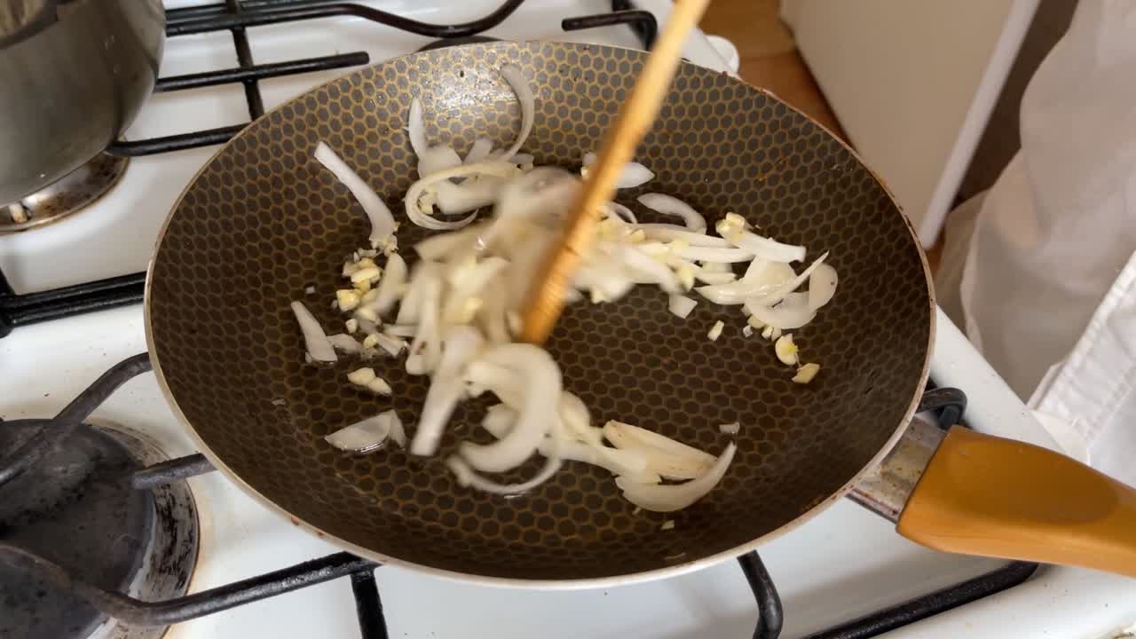 Julienne onion and garlic in a pan, stir with a wooden spoon while cooking on a gas stove