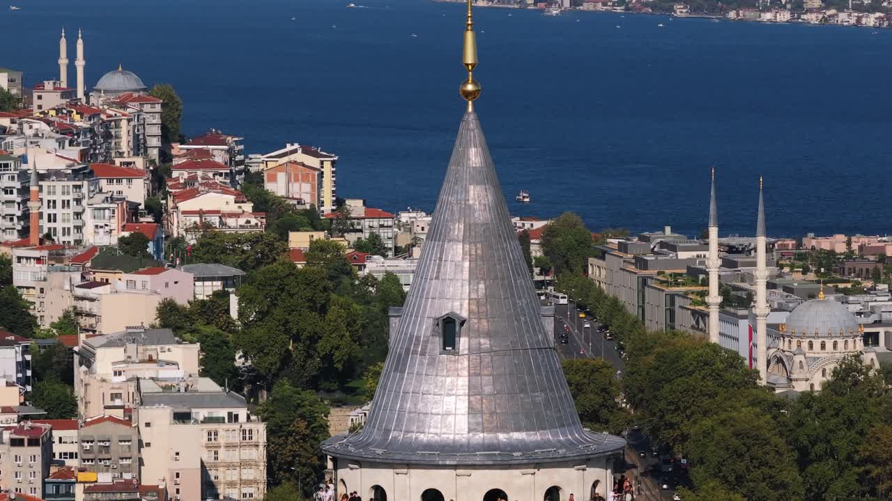 Drone Ascends, Revealing Tourists Enjoying a Panoramic View from Galata Tower Observation Deck with Bosphorus Strait in Background. Summer Atmosphere