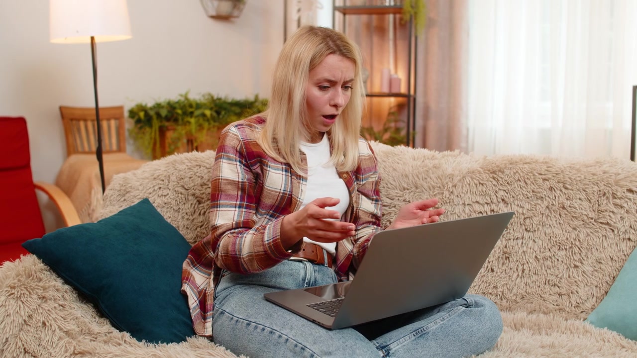 Donna adulta legge un'email con cattive notizie sul laptop a casa, reagendo con delusione e stress.