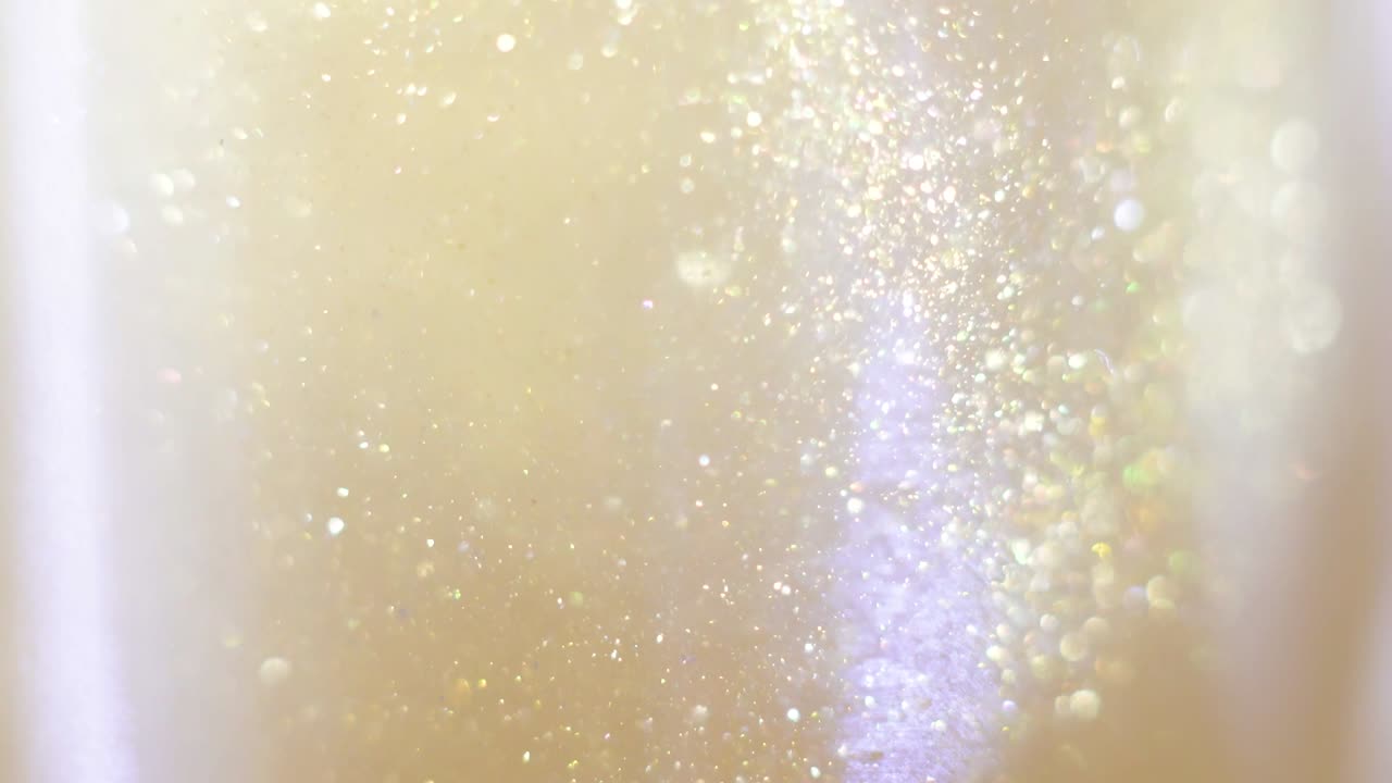 Nahaufnahme von Glitzer, der in Wodka schwebt. Farbenfrohe goldene Farbe mischt sich in Wasser. Tinte wirbelt unter Wasser. Wolke aus seidiger Tinte. Makroansicht