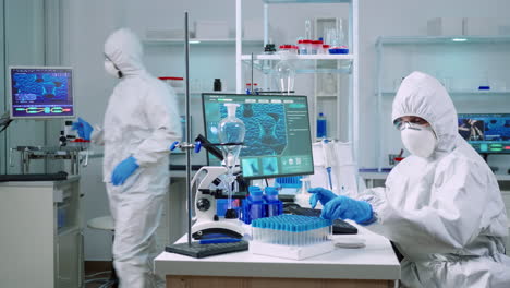 Doctor-in-coverall-taking-blood-sample-tube-from-rack-with-machines