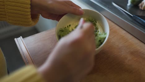 Mujer-Poniendo-Pepino-Rallado-En-Un-Tazón-De-Yogur-Griego-Para-Crear-Un-Delicioso-Tzatziki-Fresco