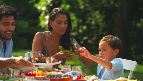 family eating outdoor meal in summer garden at home together