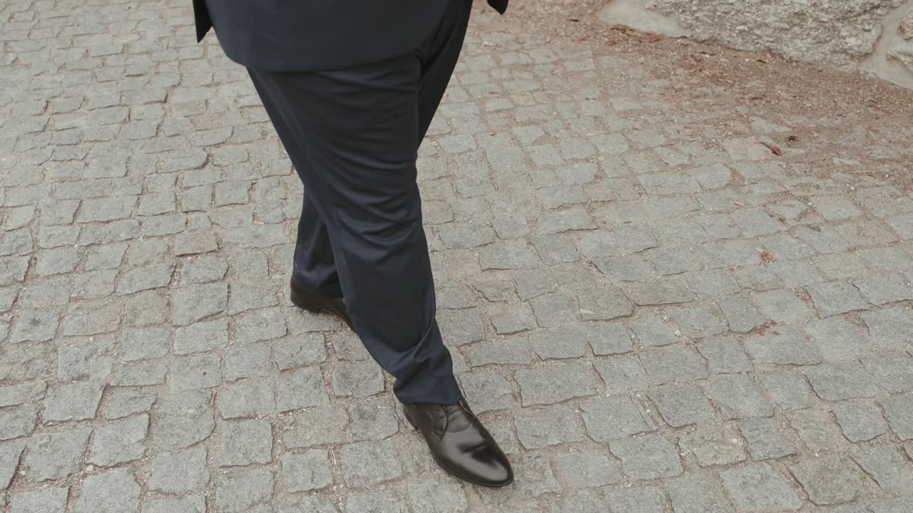 Damat, düğün töreninden önce arnavut kaldırımlı yolda kendinden emin bir şekilde yürürken cilalı siyah ayakkabıları ve pantolonu