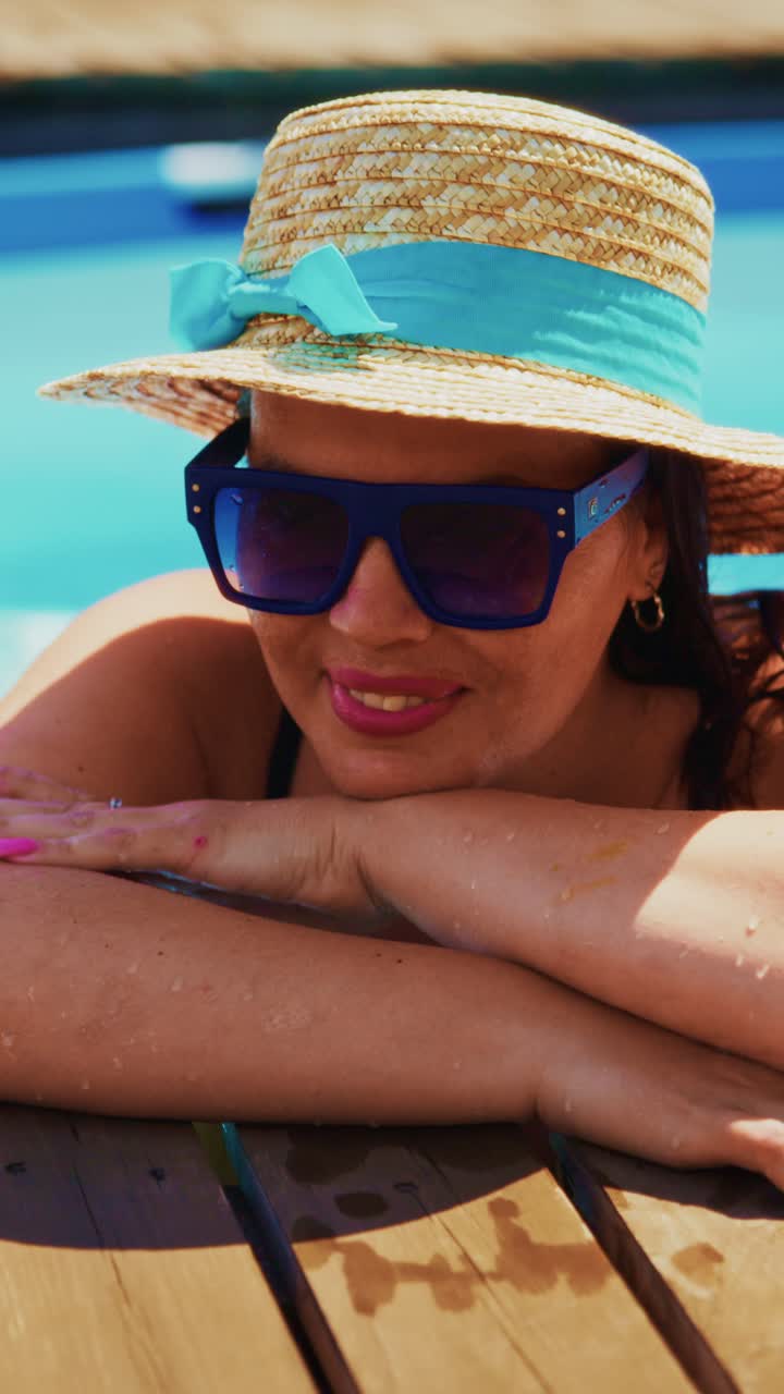 Puro relax a bordo piscina: una donna felice si gode il sole estivo con un cappello alla moda e occhiali da sole, immersa nell'acqua rinfrescante e nella serenità circostante