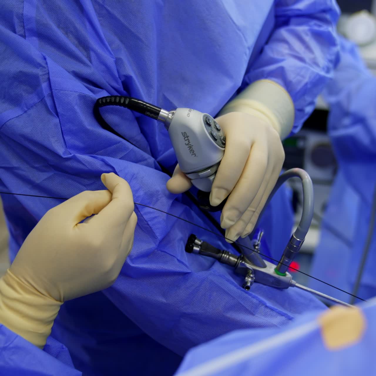 Endoscopic surgical instrument in the hands of a surgeon. Assistant's gloved hands are holding the wire from a tool