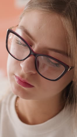 young woman in glasses looks downward in library. concentrated female student studies lesson in college class. self-preparation for exams at university