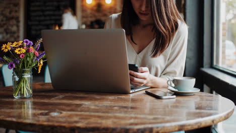 woman working on laptop and phone in a cafe