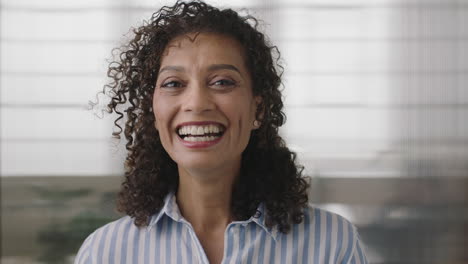 Retrato-De-Una-Hermosa-Mujer-De-Negocios-Hispana-Madura-Riéndose-Mirando-La-Cámara-Alegre-Disfrutando-De-Una-Carrera-Exitosa-En-El-Fondo-Del-Espacio-De-Trabajo-De-Oficina