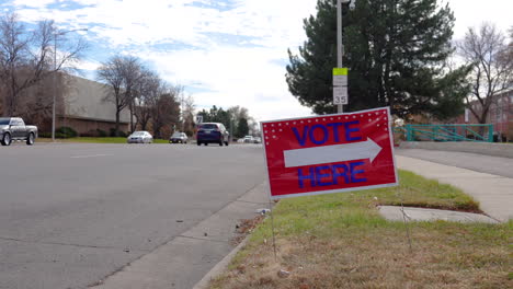 vote here sign arrow pointing left with people driving cars in background, wide