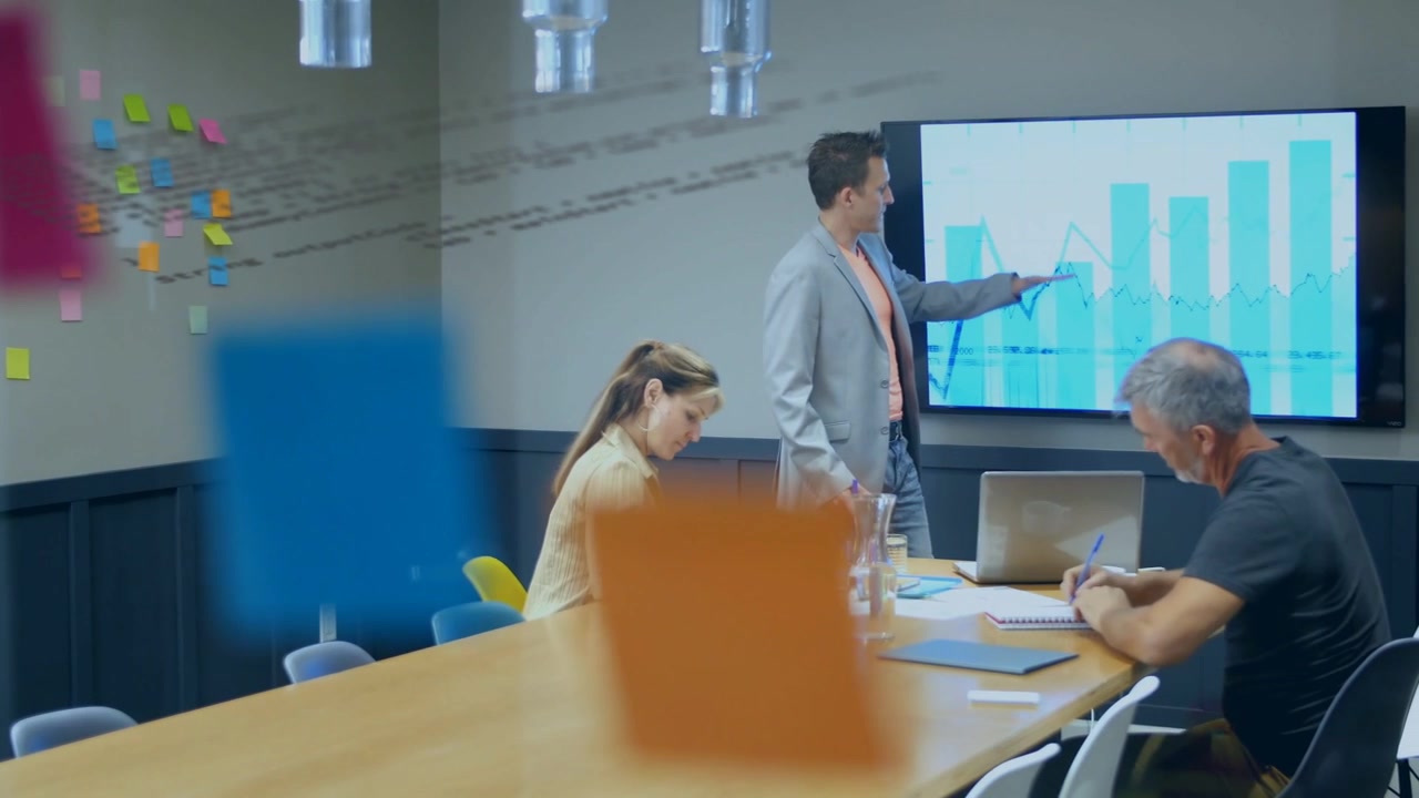 Presenter pointing at bar-line chart highlighting trends as business team writing notes, planning