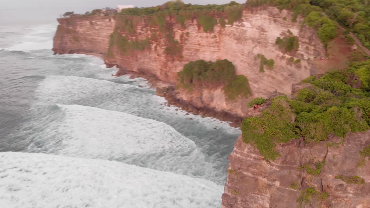 Cinematic smooth aerial drone shot of large waves crashing into huge cliff edge in uuwatu, Bali during golden hour on summer sunset-2