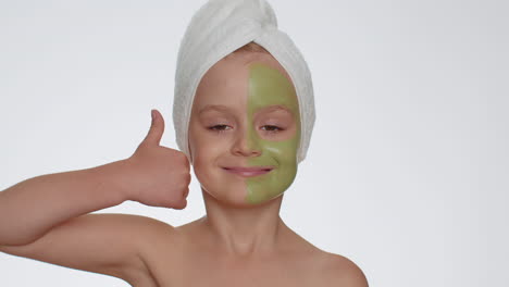 lovely smiling child girl kid in towel on head applying cleansing moisturizing green mask on face