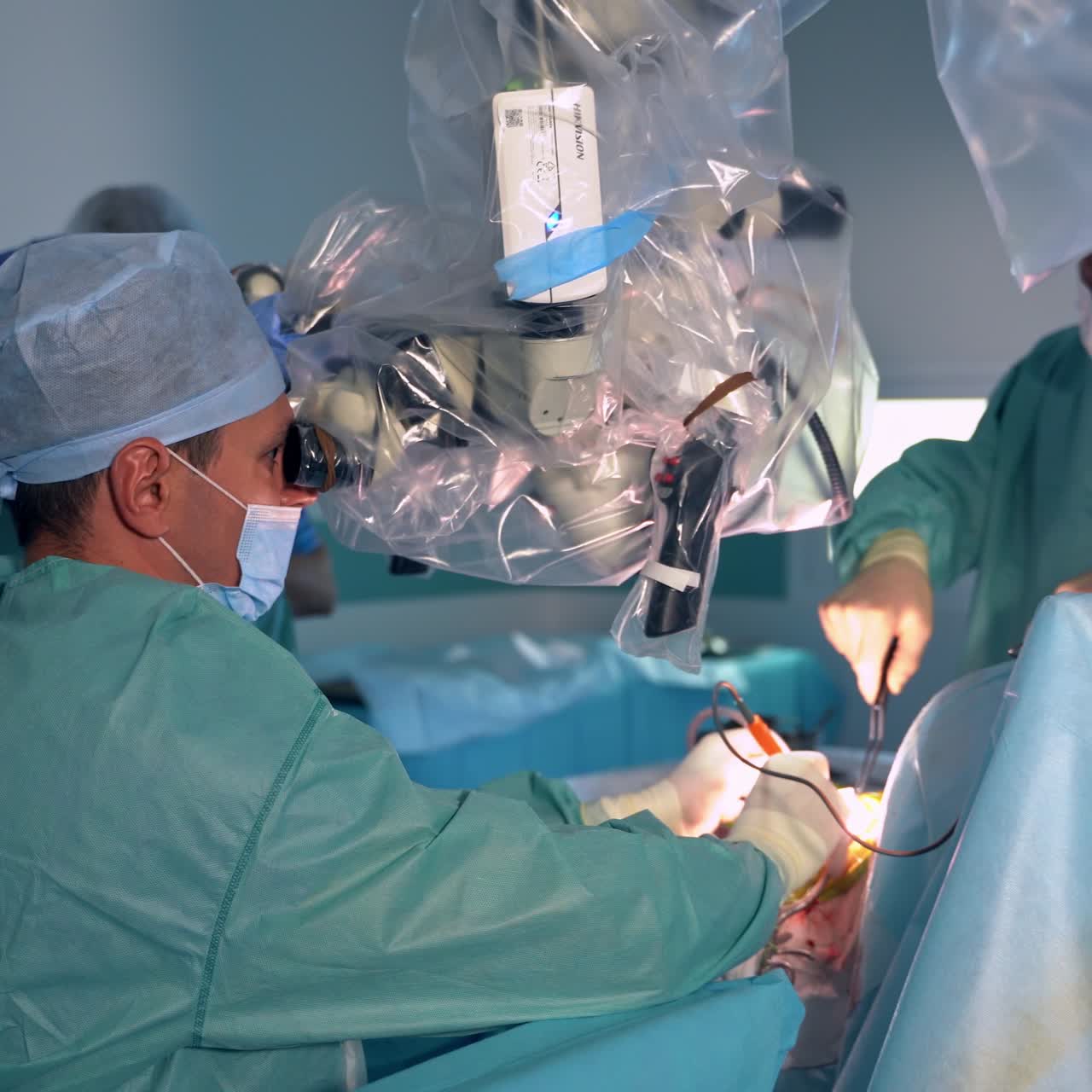Surgeon stretched hands holding instruments operating the patient. Doctor looks carefully into microscope hanging over the table