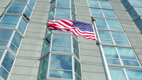 american flag on flagpole in front of city building waves in the breeze in slow motion