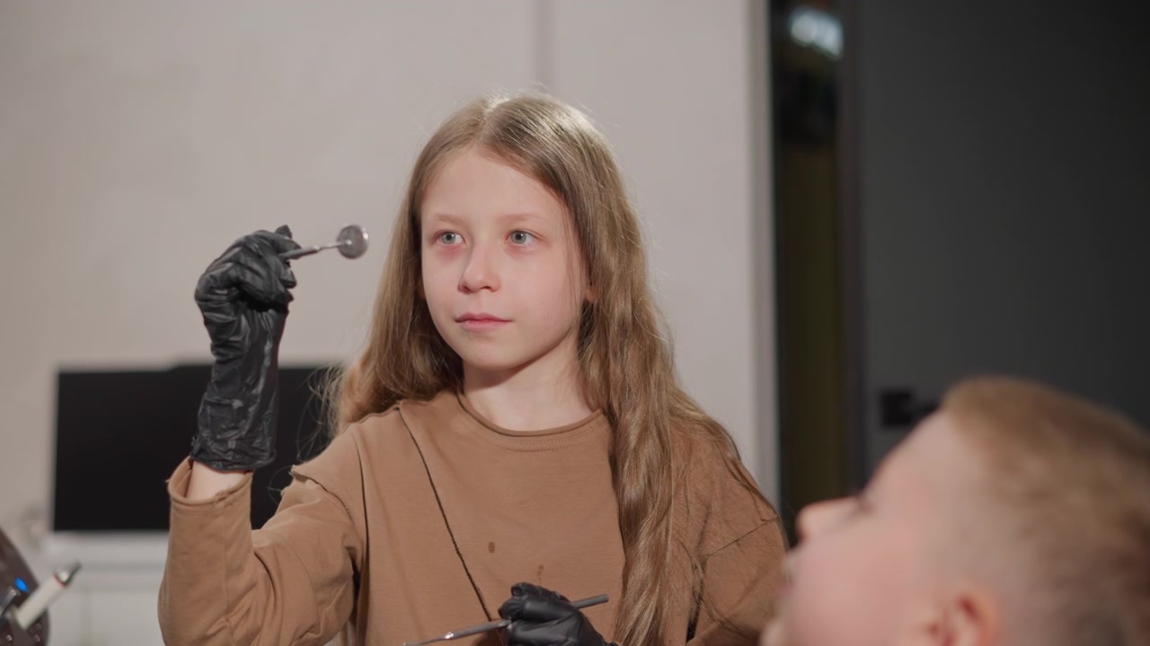 Primo piano di giovane ragazza che indossa guanti neri e tiene strumenti dentali durante una procedura ortodontica. La scena mostra un ambiente clinico con un'altra ragazza parzialmente visibile, enfatizzando l'aspetto medico.