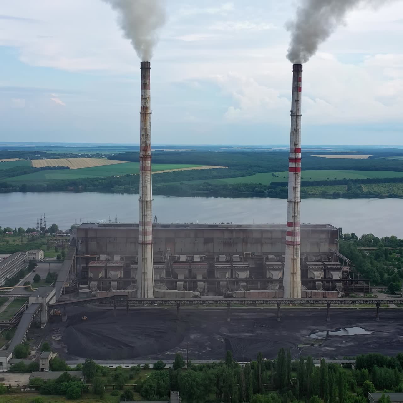 Factory building with smoking pipes. Industrial territory situated near the river. Harmful smoke from manufacture pollutes the atmosphere in nature. Aerial view