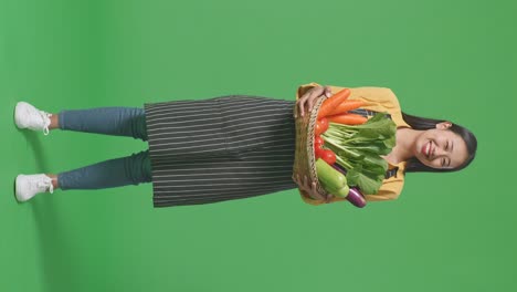 full body of asian female farmer carrying a vegetable basket warmly smiling on green screen background in the studio