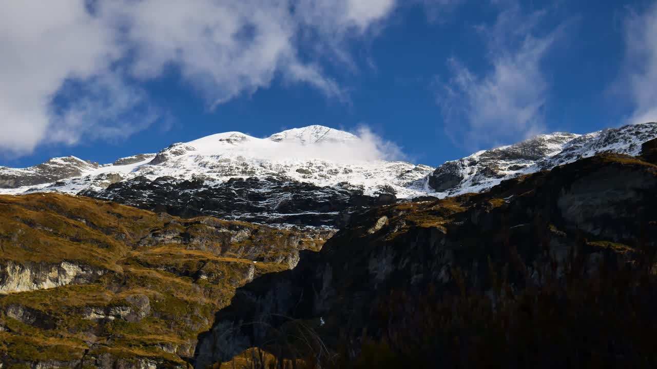 toma de lapso de tiempo de nubes voladoras contra el cielo azul sobre montañas nevadas a la luz del sol