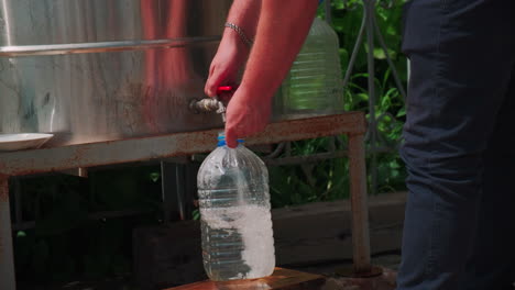 person filling plastic bottles with water from a large container