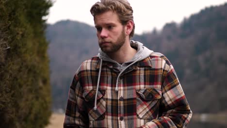 a young blond man touches a shrub thoughtfully, lost in contemplation