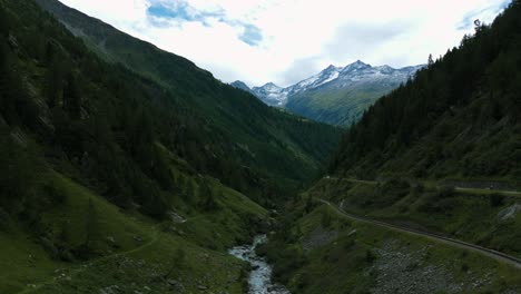 Vista-Aérea-Del-Valle-Del-Paso-De-Furka-Y-Del-Arroyo-Que-Fluye-En-Suiza-Con-Picos-Montañosos-En-El-Fondo