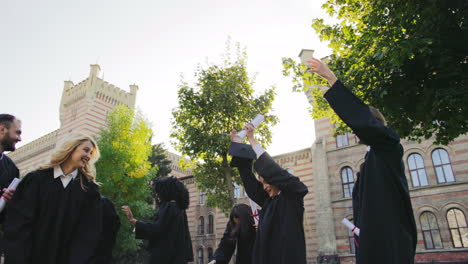 group of multi ethnical female and male graduates tossing their black caps up in the air cheerfully on the graduation day