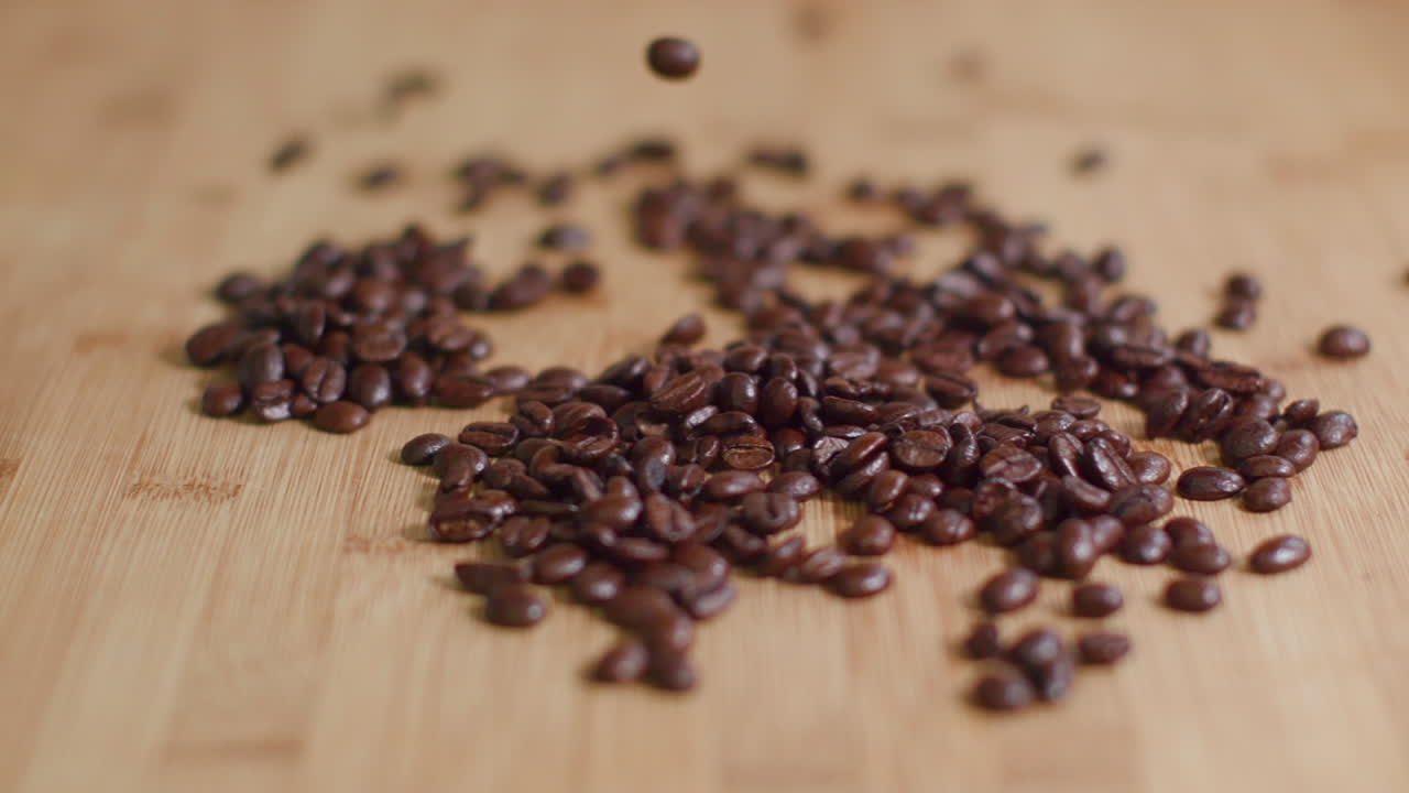 Coffee Beans Dropping into Pile on Wooden Surface in Slow Motion