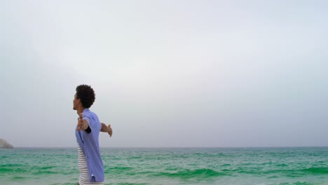 Rear-view-of-African-American-man-standing-with-arms-outstretched-on-the-beach-4k