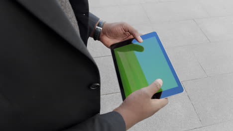 businessman browsing internet on tablet outdoors. worker using pad on street