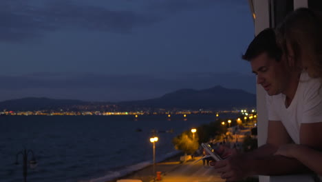 Man-and-woman-with-pad-on-balcony-at-night