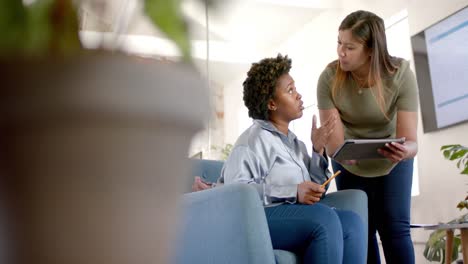 diverse business female colleagues in discussion using tablet in casual office meeting, slow motion