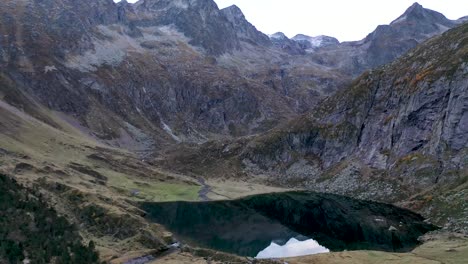 Lac-d'Espingo-mountain-lake-with-calm-water-located-in-Haute-Garonne,-Pyrénées,-France,-Aerial-slow-flyover-approach-shot