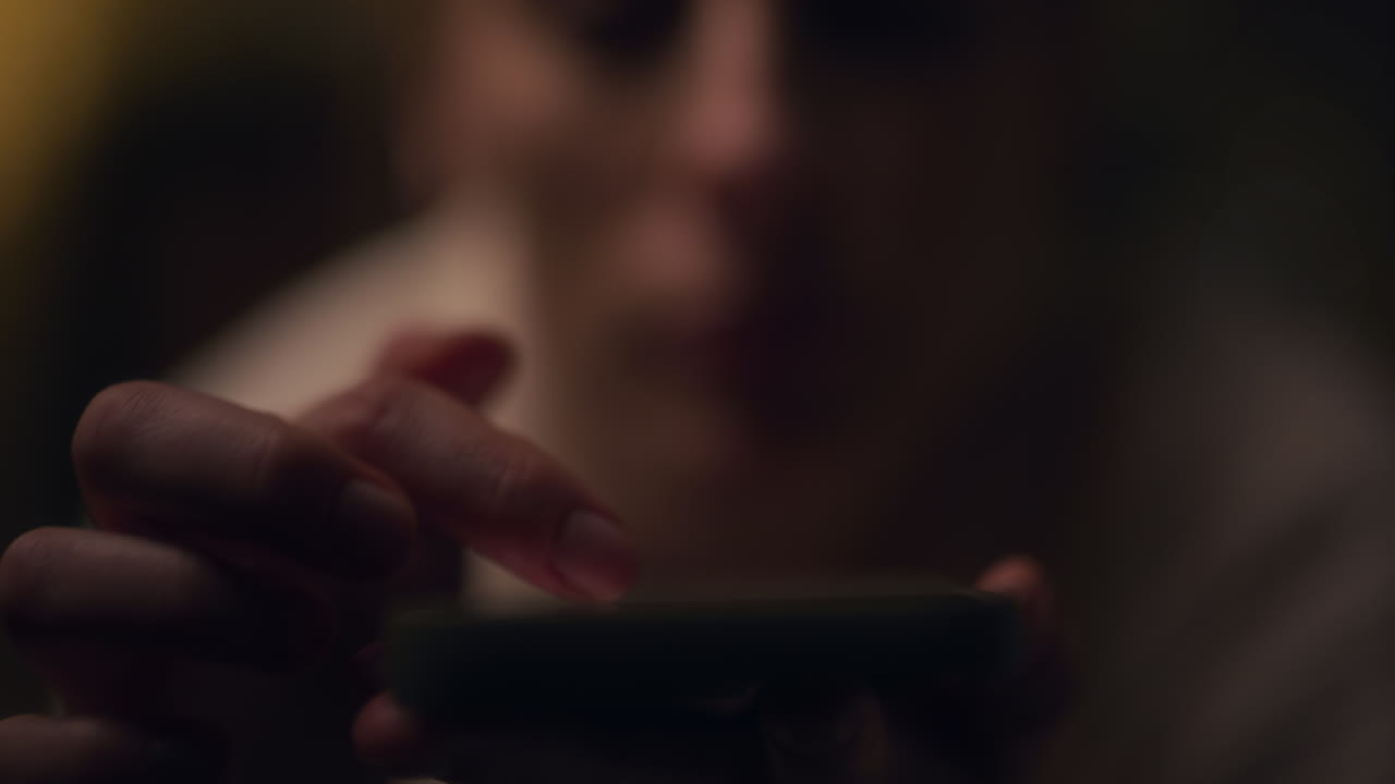 primer plano de la mano de una mujer que es adicta a las redes sociales y el teléfono inteligente y navega por internet por la noche en la luz oscura
