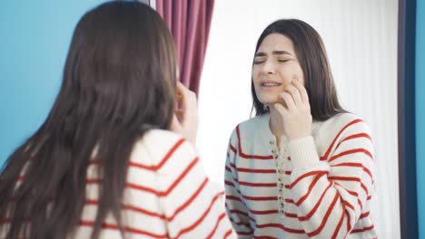 Unhappy-young-woman-looking-at-braces-in-mirror.