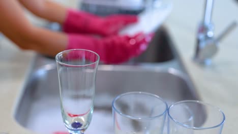 hands in pink gloves wash dishes in a bright kitchen. focus on cleaning technique and organized environment