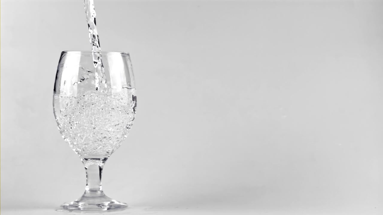 Acqua limpida versata in un bicchiere su sfondo bianco.