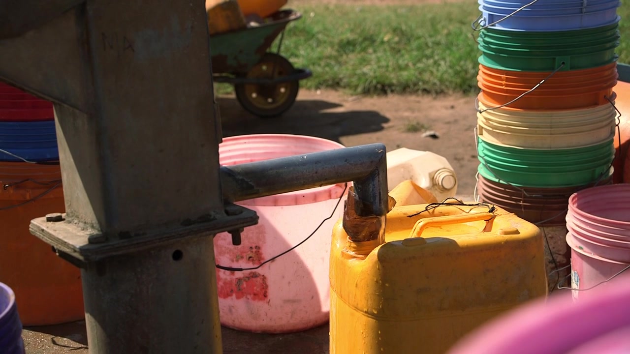 Handpump och färgglada vattenbehållare vid en lantlig vattenpost i Moçambique.
