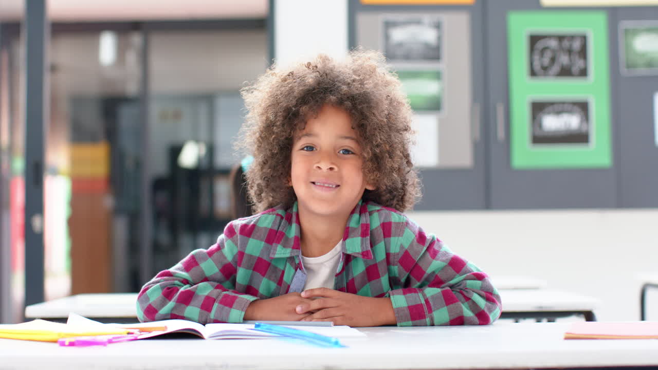 Smiling girl sitting at desk with open notebook and pencils in school classroom