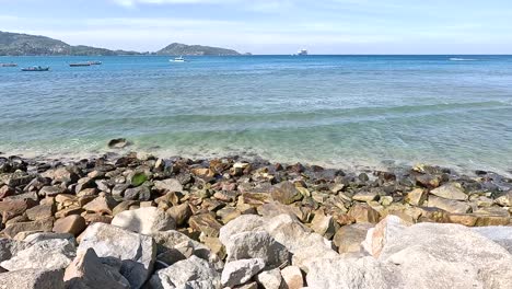 gentle waves lap against rocky shores under clear skies at kalim beach, phuket. the tranquil scene captures the essence of coastal serenity